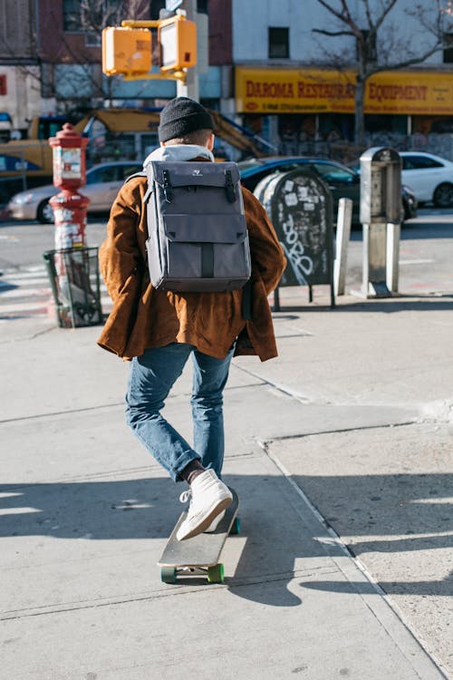 Homem Vestindo Jaqueta Marrom, Jeans Azul E Sapatos Brancos Andando De Skate Na Lateral