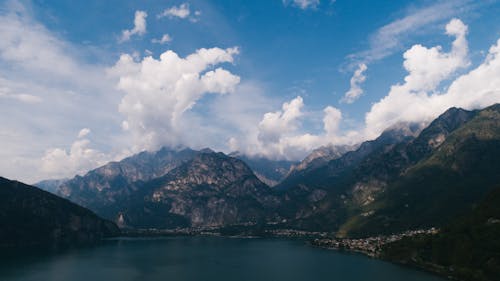 Green and Brown Mountains Beside Body of Water Under Blue and White Cloudy Sky