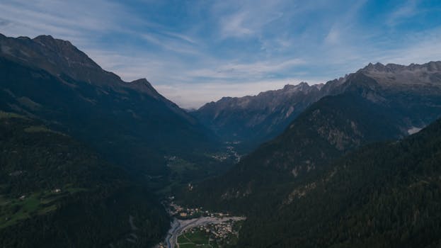Drone shot capturing a tranquil mountain valley with lush greenery and a distant village.