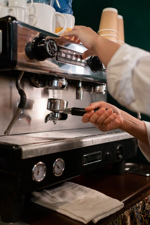 Free Hands of a barista operating an espresso machine, preparing coffee in a cozy cafe setting. Stock Photo