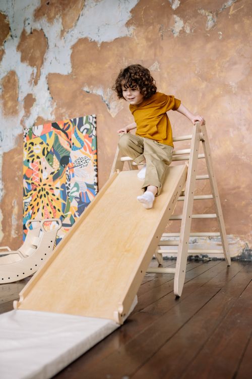 Free Young child playing on a wooden slide inside a colorful room. Stock Photo