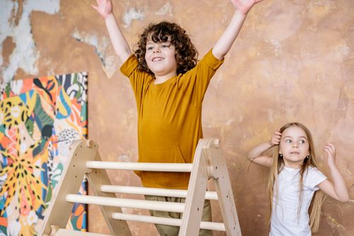 Free Two cheerful kids playing on a wooden ladder indoors, expressing excitement and fun. Stock Photo