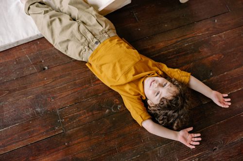 Free A happy child with curly hair lies smiling on a wooden floor, enjoying a carefree moment. Stock Photo