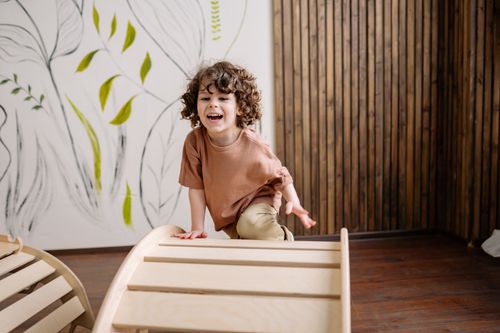 Free Joyful child with curly hair enjoying a playful moment indoors on a wooden structure. Stock Photo
