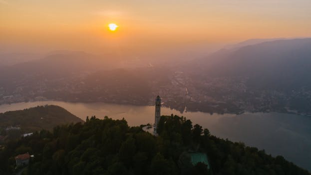 Aerial view of a serene sunset over a lake with a prominent tower and lush landscape.