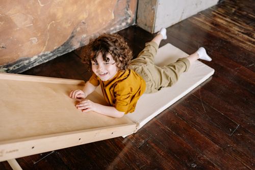 Free Curly-haired child smiling while playing on a slide indoors. Stock Photo