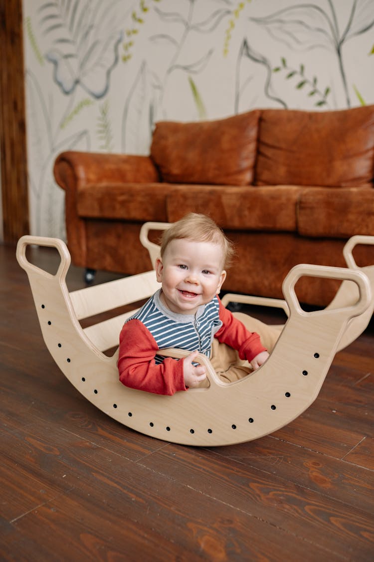 A Cute Baby Boy Sitting On A Wooden Rocker