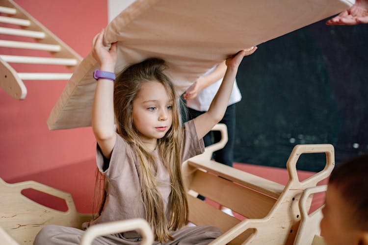 A Girl With A Cushion On Her Head While In A Wooden Rocker