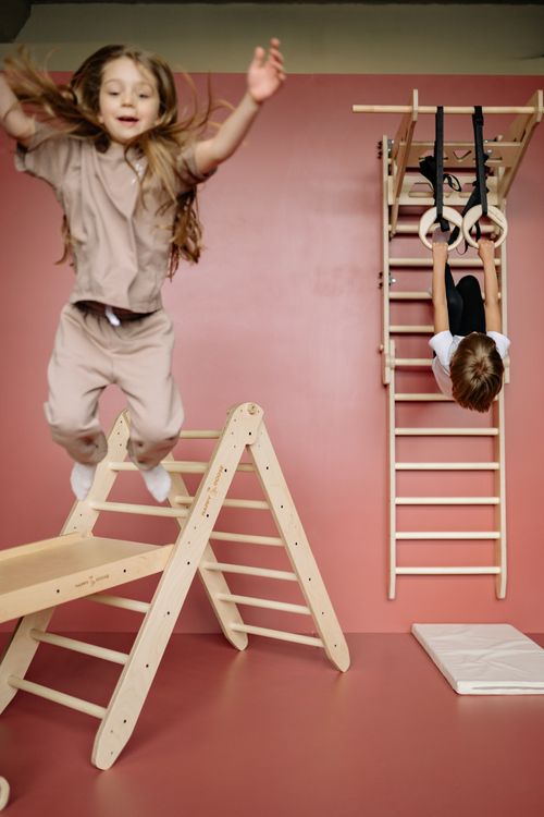 Free Kids enjoying indoor playtime on wooden gym equipment, jumping and swinging with fun and energy. Stock Photo