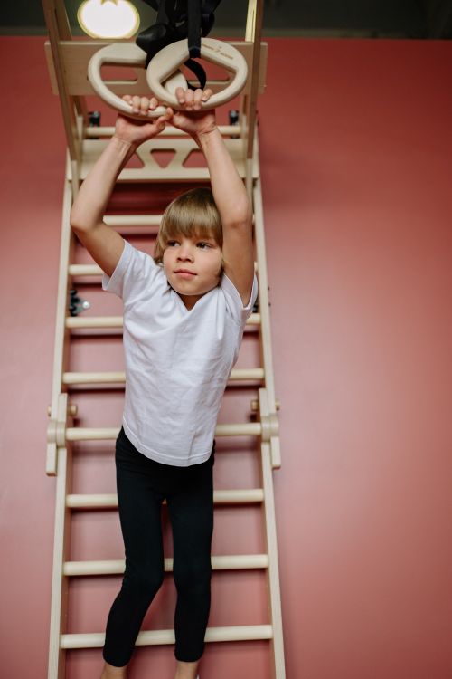 Free Child with blond hair hangs on gymnastic rings indoors on a wooden ladder. Stock Photo