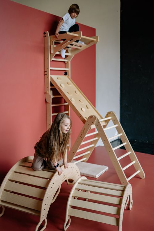 Free Kids enjoying a wooden climbing frame indoors, fostering fun and activity. Stock Photo