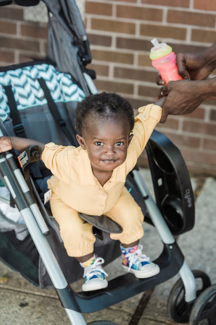 Child In Yellow Clothes Sitting In A Baby Stroller