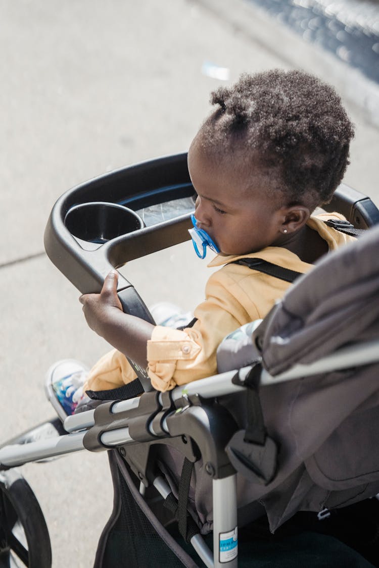 A Child With A Pacifier Sitting In A Baby Stroller