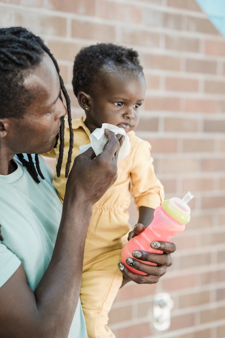 Man Holding A Feeding Bottle Wiping A Child's Face