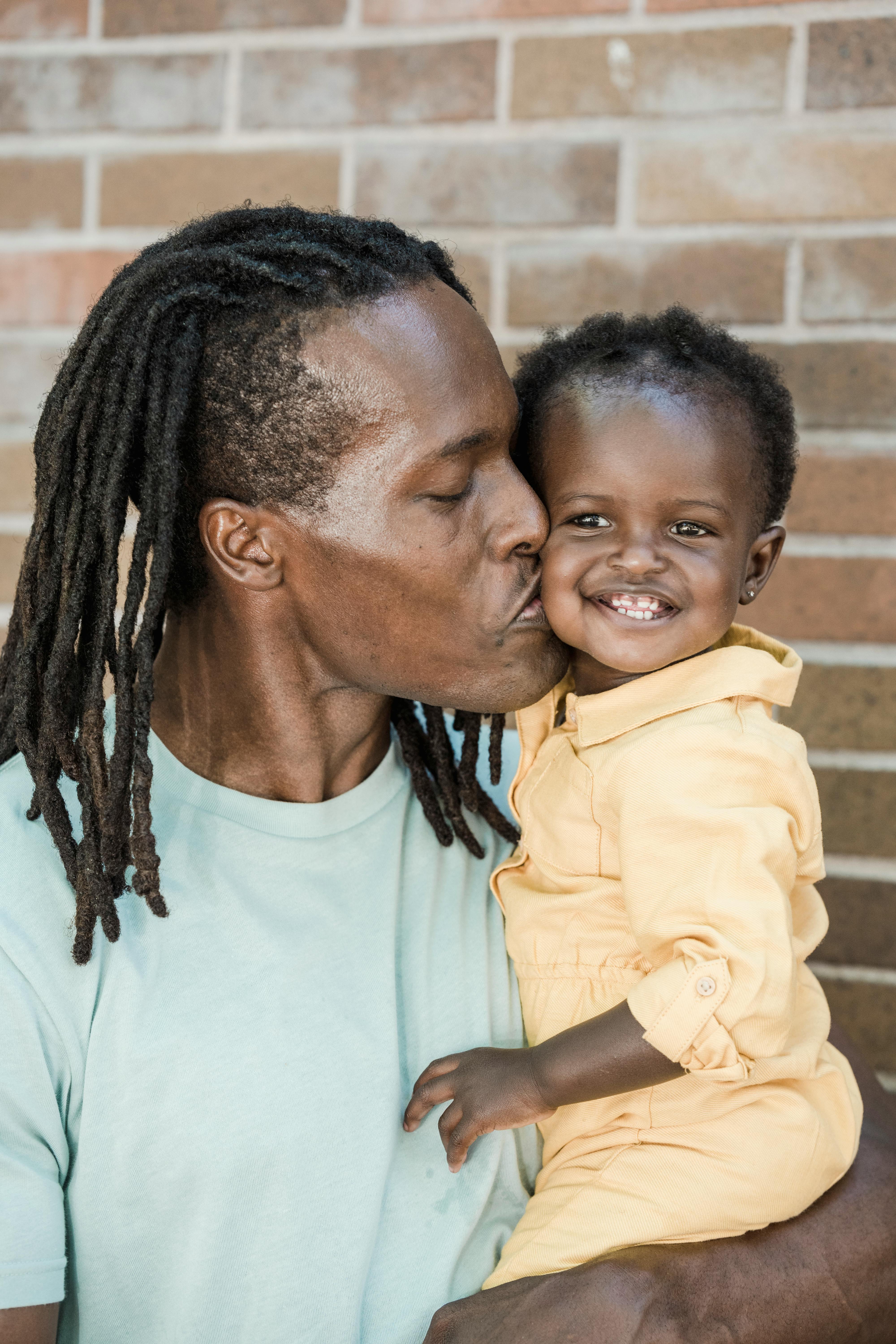 man with dreadlocks in a green shirt kissing a child