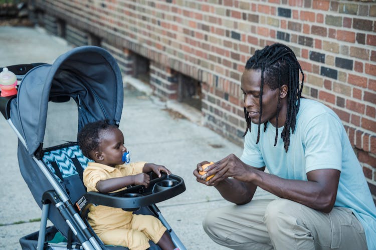 Man Peeling An Orange Next To A Child In A Baby Stroller