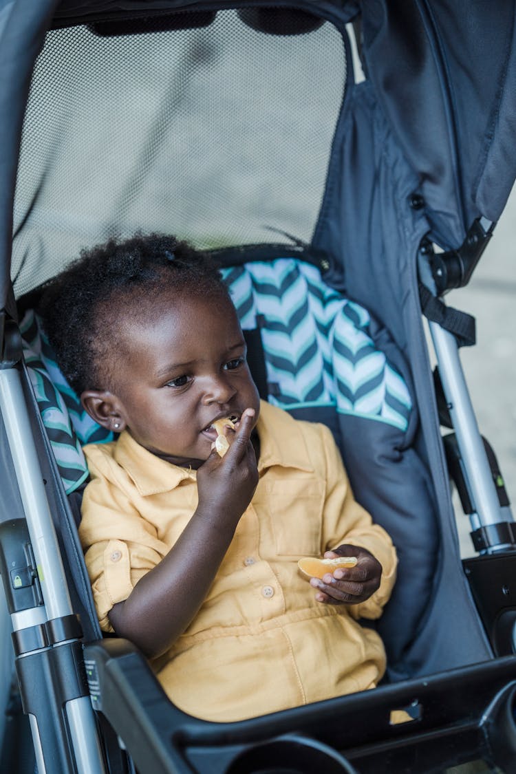 A Child In Yellow Jumpsuit Eating Oranges