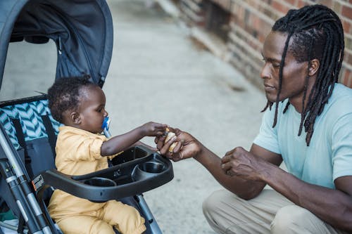 Father Sharing Food with His Daughter Sitting in a Stroller 