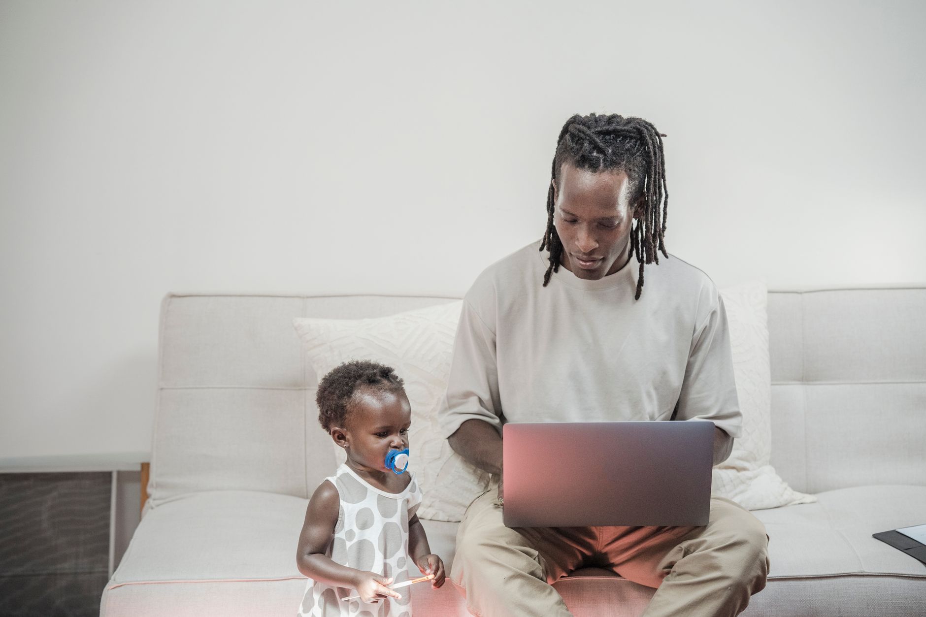 A father working on a laptop at home as his toddler daughter sits beside him, highlighting family balance.