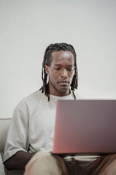 Adult man sitting indoors using a laptop, representing modern technology and work flexibility.