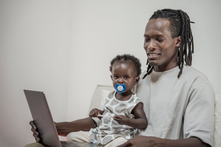 Father Watching Something On A Laptop With His Baby Daughter 