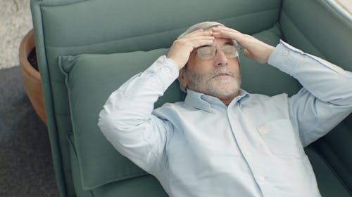 Elderly Man in Blue Dress Shirt Lying on Green Couch