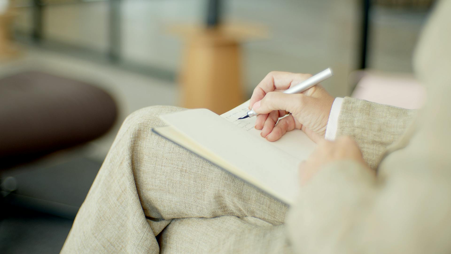 Close-up of a person writing in a notebook with a pen, indoors.