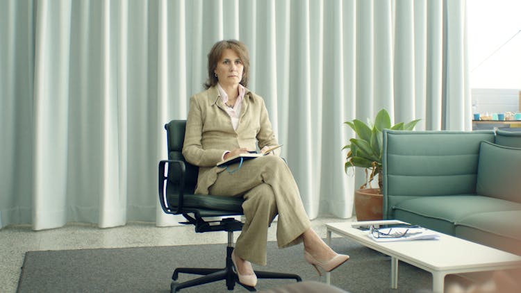 Woman In Brown Coat Sitting On Black Office Rolling Chair