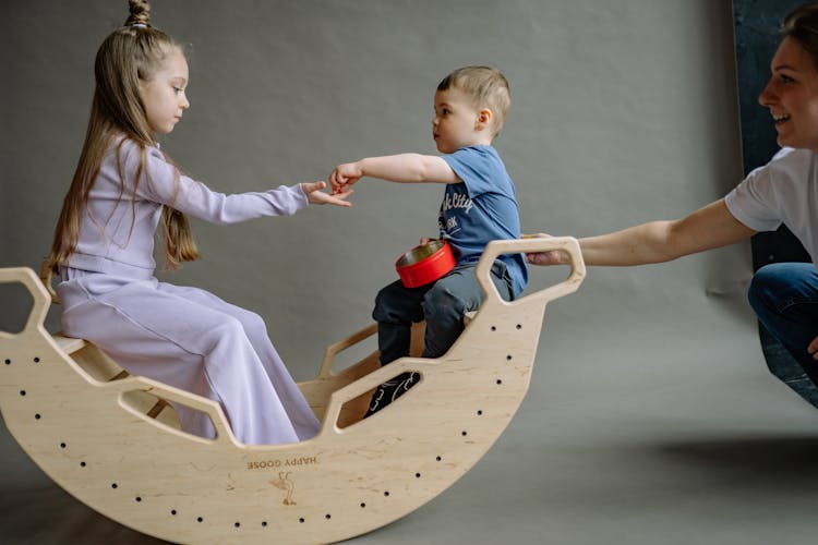 Woman Swinging Children On A Wooden Toy