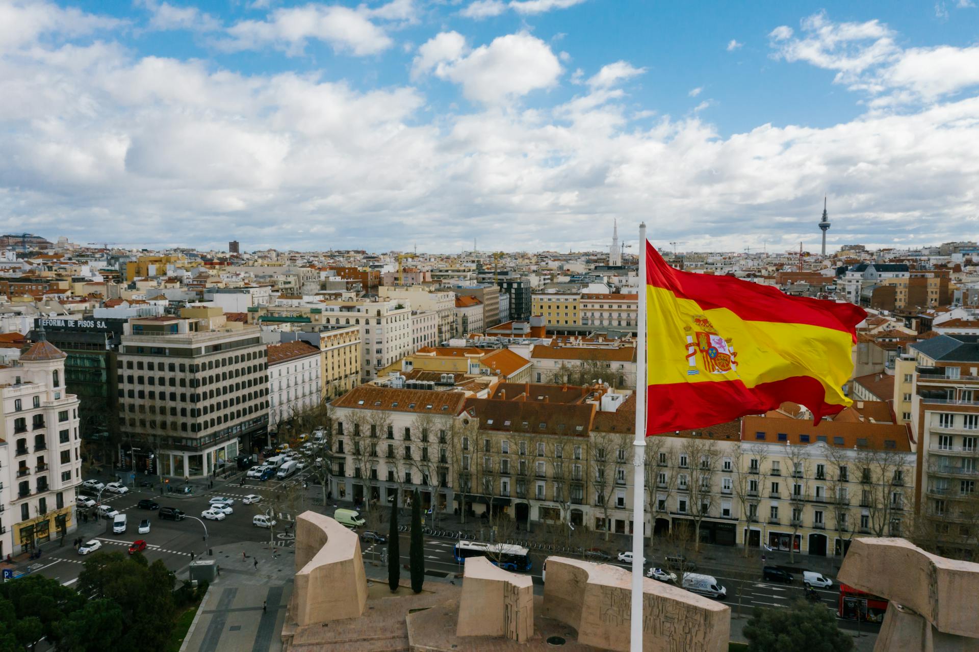 Uitzicht vanuit een drone op een Spaanse stad met oude gebouwen en de nationale vlag onder een bewolkte blauwe hemel