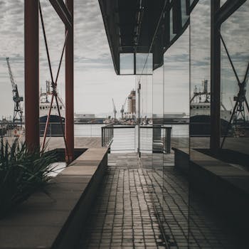 A modern harbor view with industrial ships and reflective architecture on a cloudy day.
