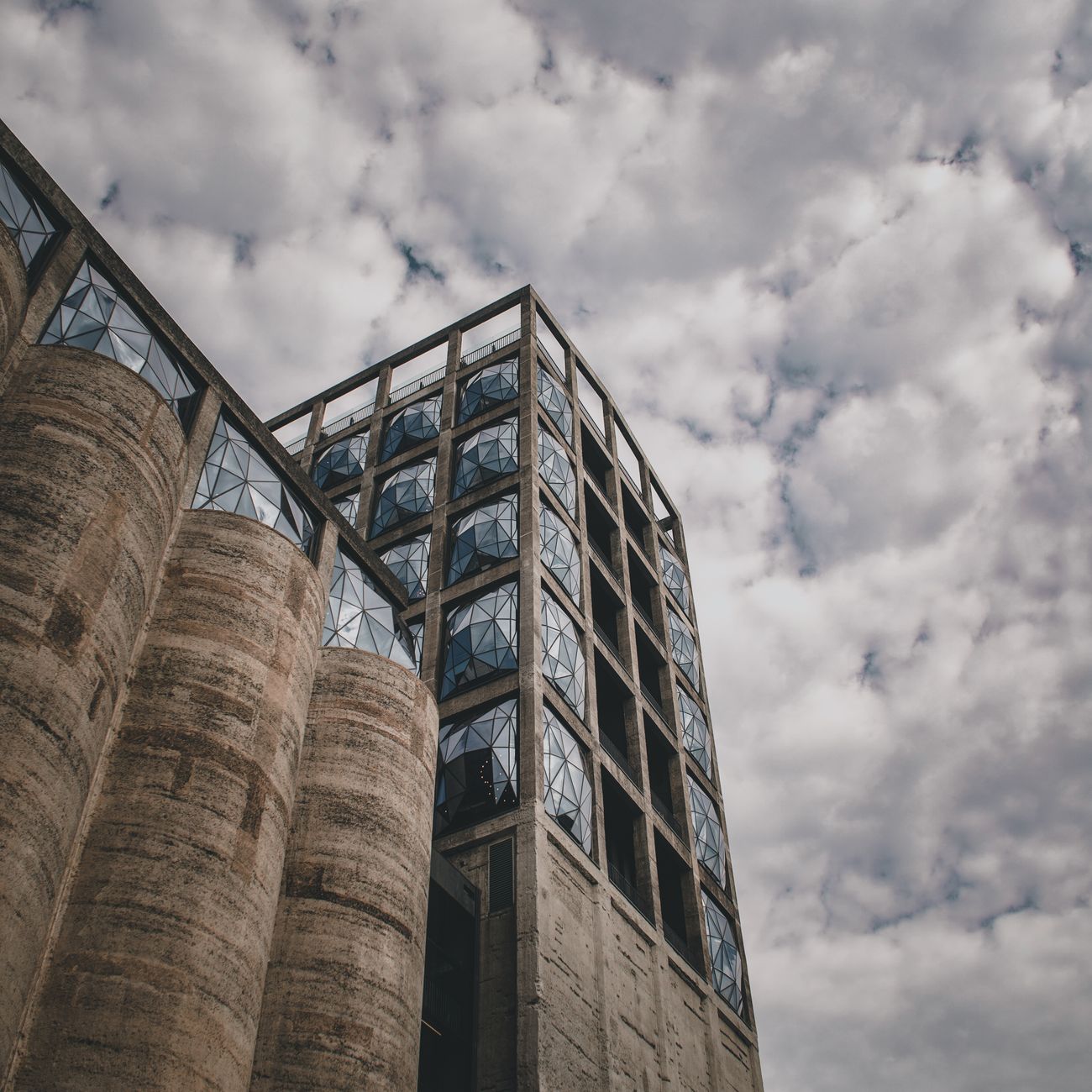Low-angle shot of a modern concrete structure with geometric windows against a cloudy sky.