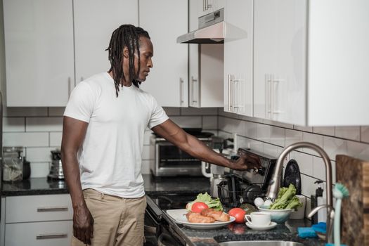 A man in a white shirt prepares breakfast in a stylish kitchen with fresh vegetables.