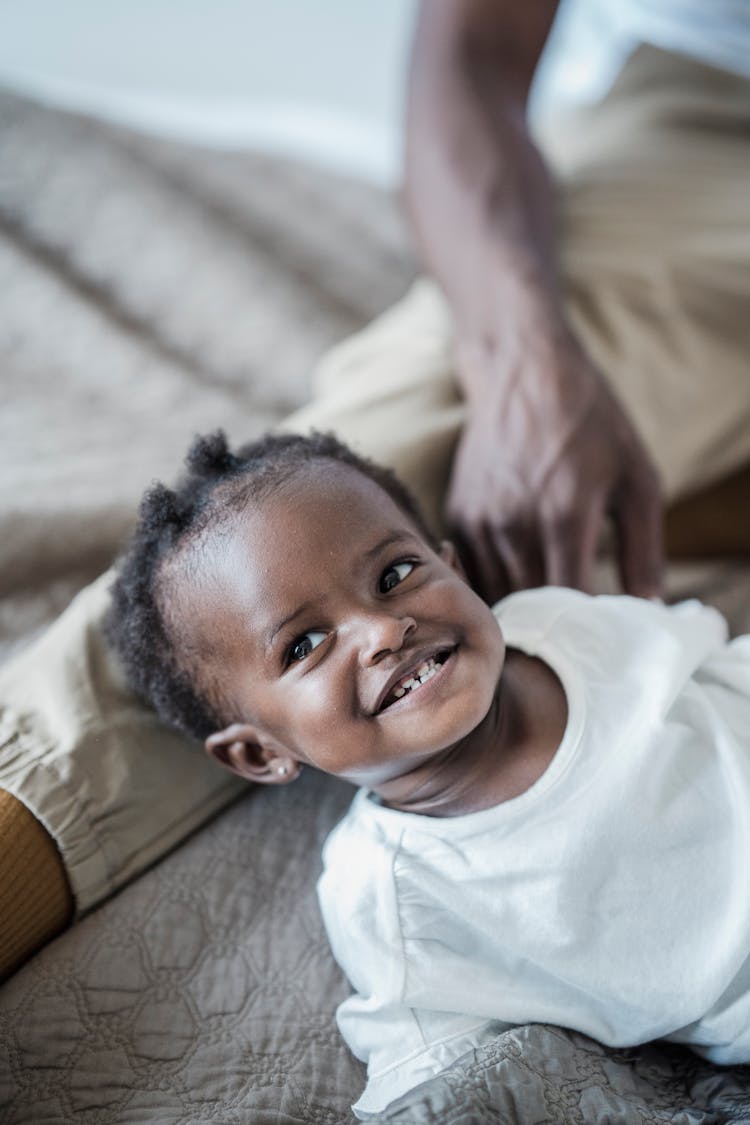 Portrait Of A Smiling Baby Girl Lying Down On Bed