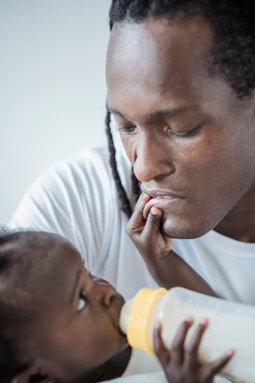 Free Child Touching His Father's Lips While Drinking Milk From a Baby Bottle Stock Photo