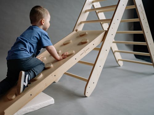 Little Boy Climbing Up a Wooden Climbing Wall on an Indoor Playground 