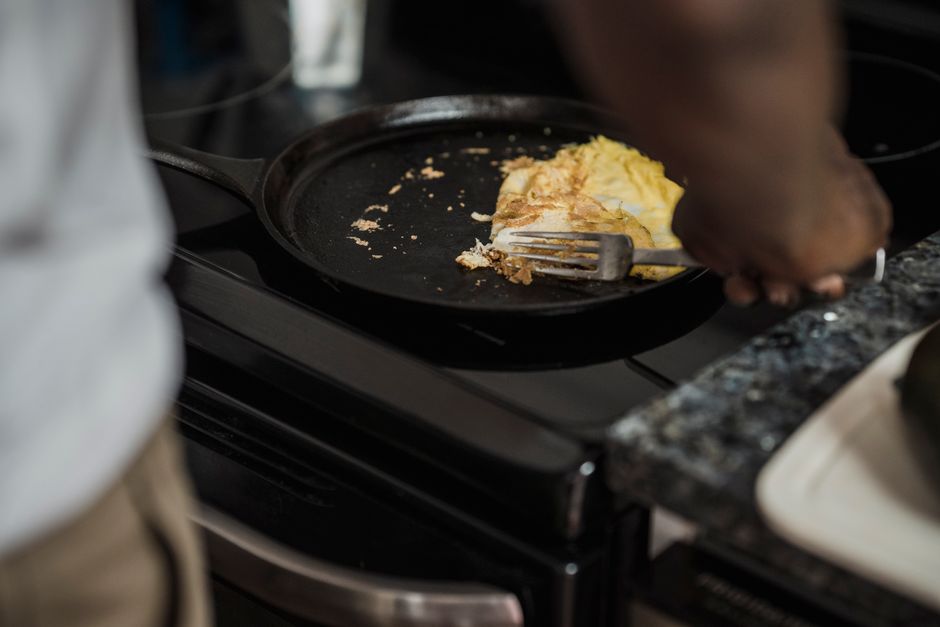 A hand using a paper towel to rub a thin layer of oil into a black cast iron skillet, its surface dark and glossy from previous seasoning.
