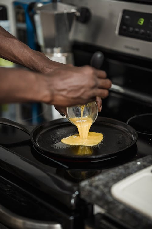 Photo of a Person Pouring Scrambled Eggs on a Black Frying Pan