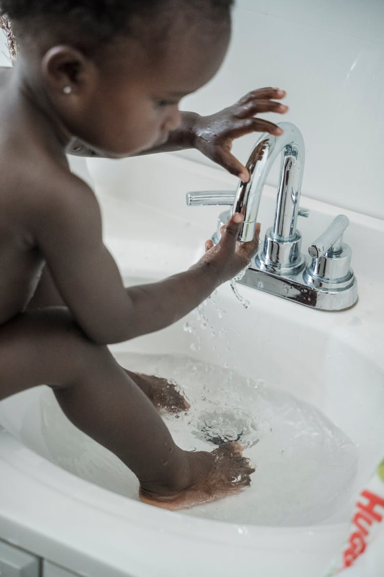 A Child With Her Feet In A Washbasin Filled With Water