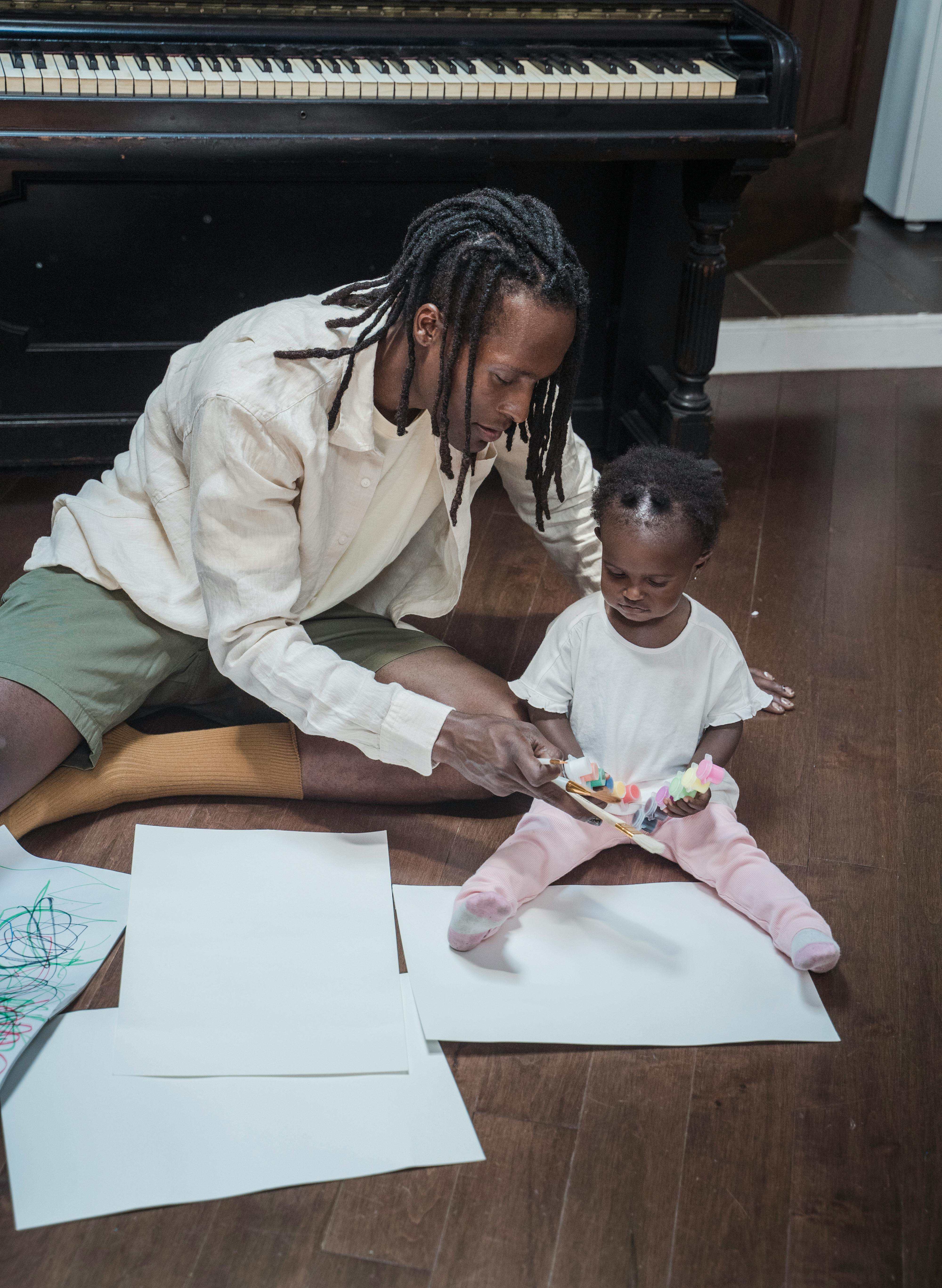 father and daughter playing on a floor with colours and piano in background