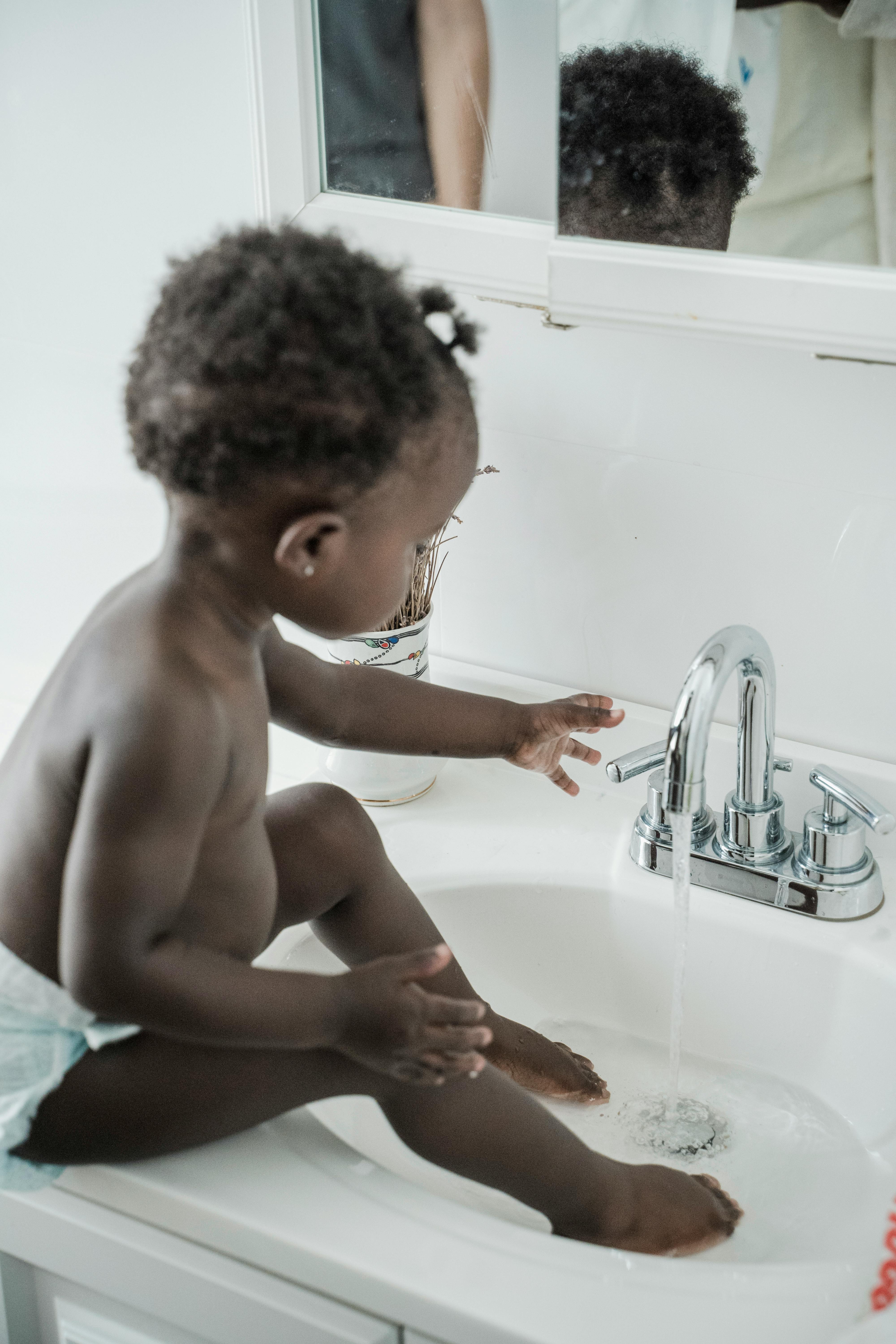baby girl soaking feet in a sink and playing with a tap