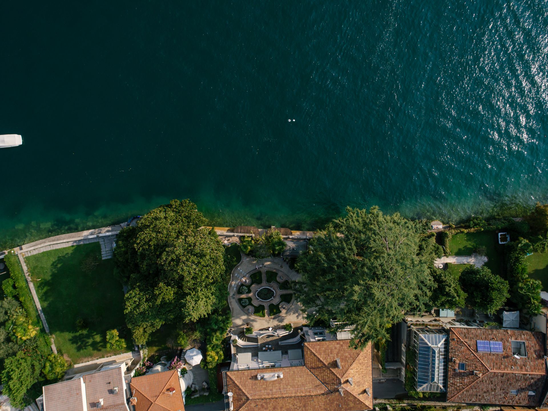 Drone shot of beautiful coastal homes with lush gardens by the vibrant ocean.