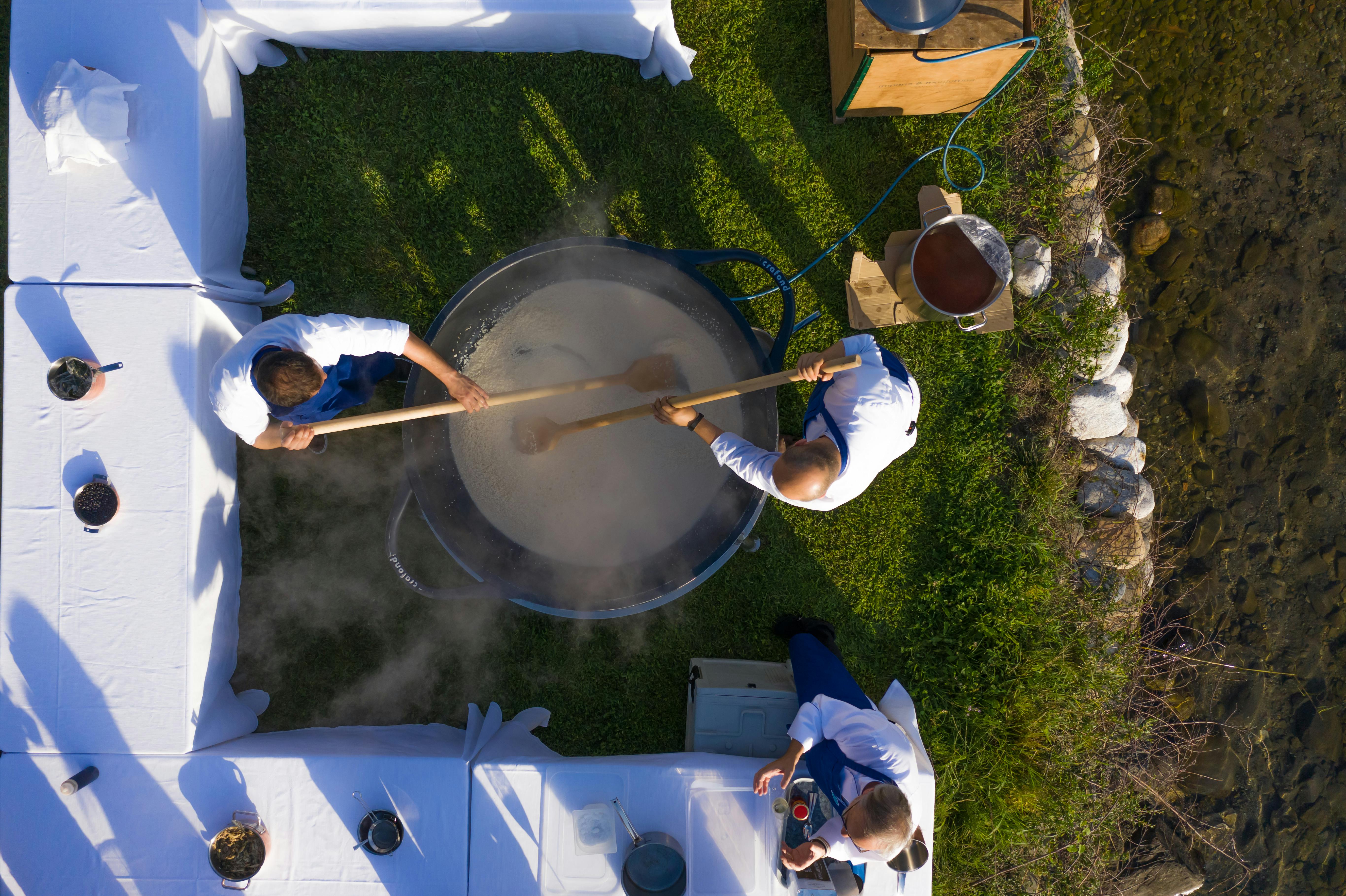 A smiling group of church volunteers in aprons serving food from large pots at an outdoor fellowship event in Ho