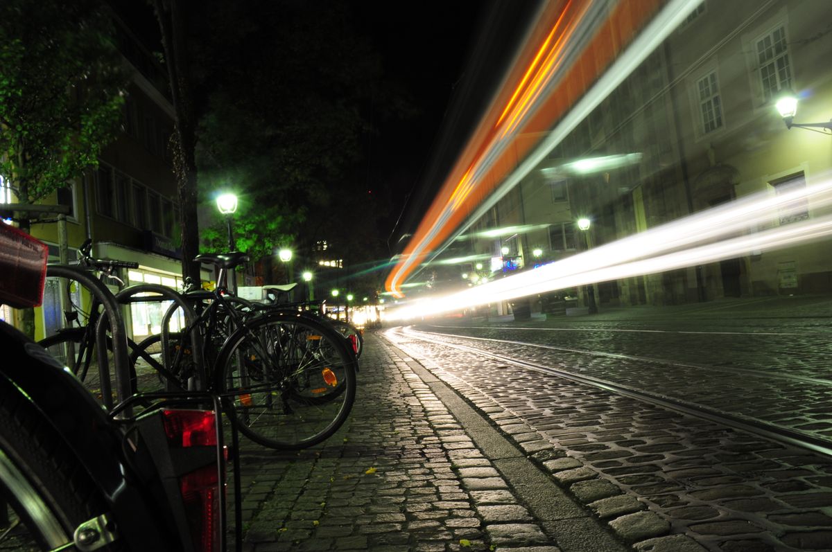 Parked bikes and light trails on a cobbled street at night — photo by Hannes L. on Pexels