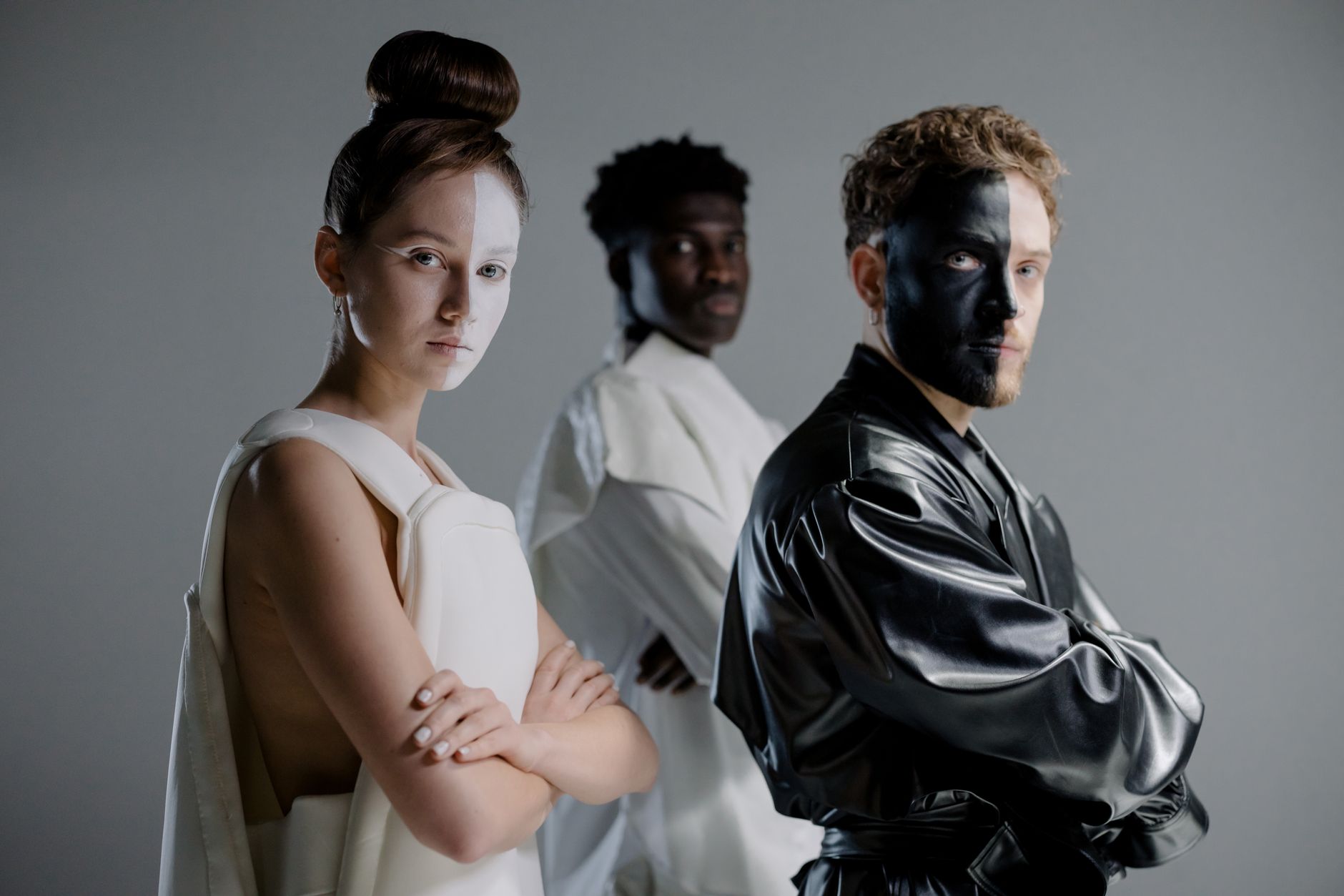 Three models posing in a studio, showcasing avant-garde fashion with striking makeup.
