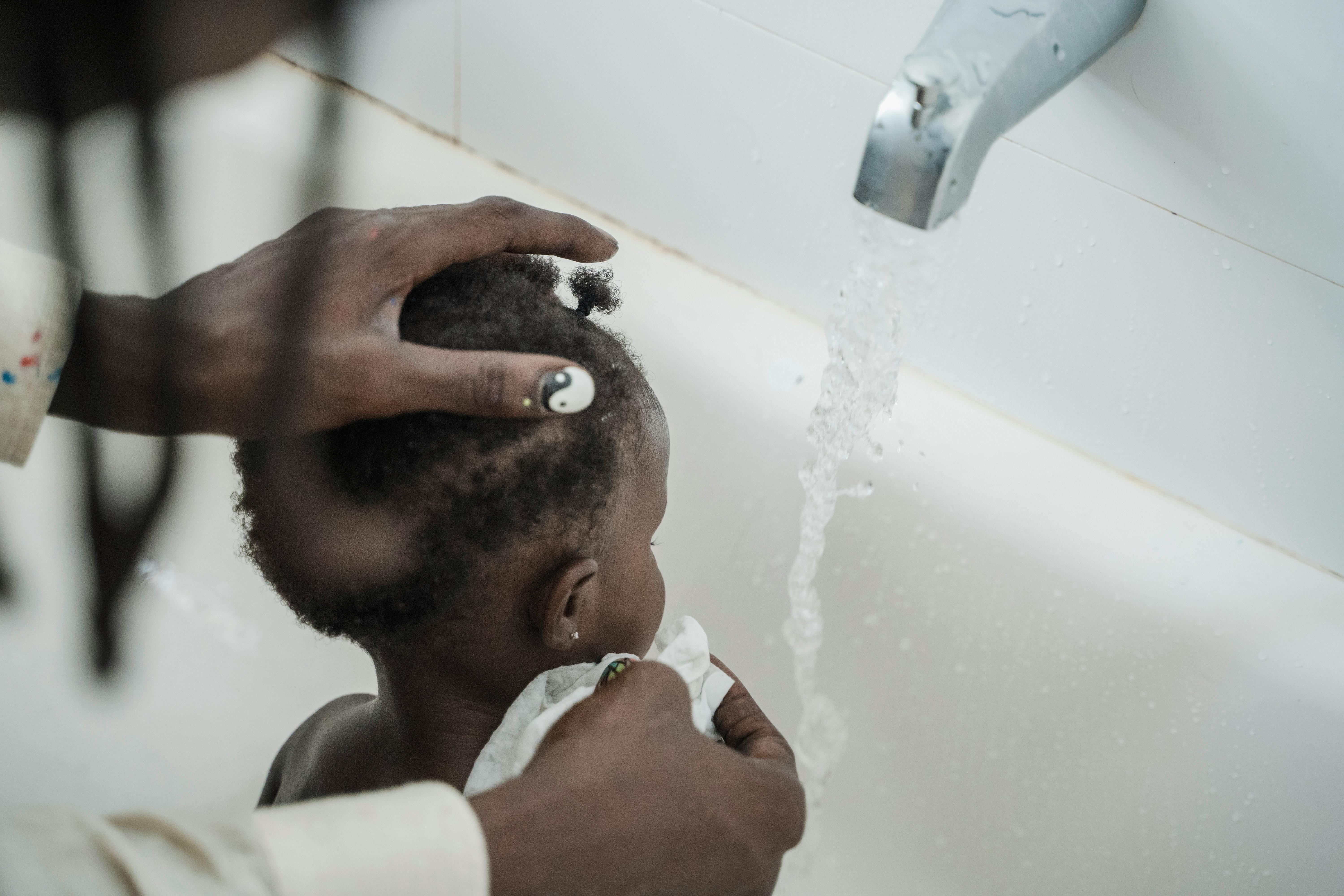 A tender moment of a father washing his baby in the bathtub, with water running from the tap.