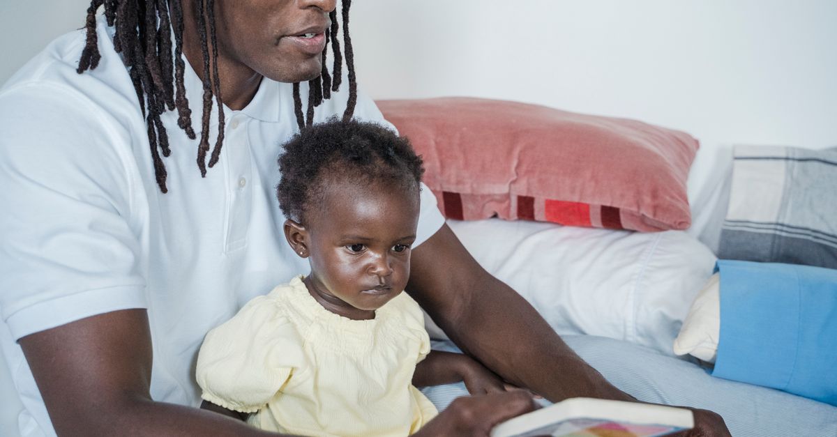 A father and his baby engage in quality time reading a book indoors, promoting bonding and learning.