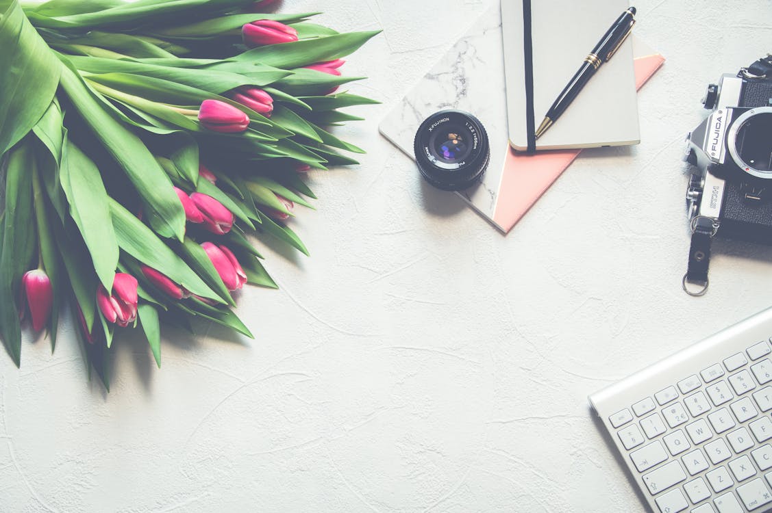 Bouquet De Fleurs De Tulipe Rose Près De Téléobjectif Noir Et Clavier D'ordinateur Argenté