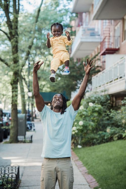 Free A playful father and daughter enjoying a joyful moment outdoors in a neighborhood. Stock Photo