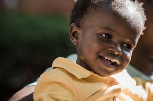 Free Close-up of a happy baby smiling warmly in a sunny outdoor setting. Stock Photo